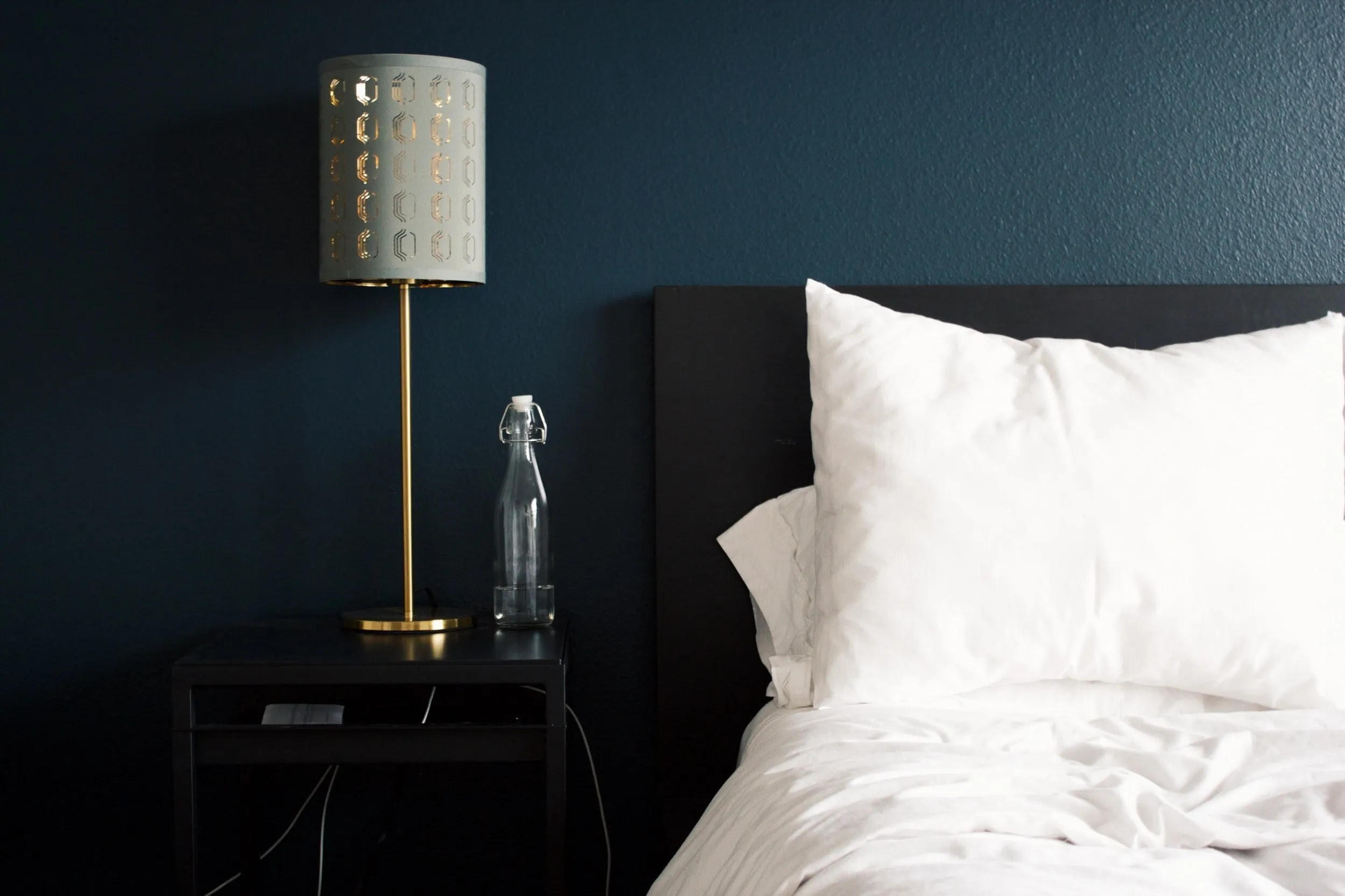 Comfortable hotel room bed with white pillows, bedside lamp, and water bottle, suggesting a restful stay for eye surgery recovery in Brisbane.