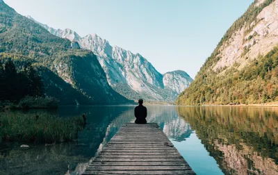Person on a wooden dock gazing across a serene lake reflecting towering mountains under a clear sky, symbolizing improved vision.