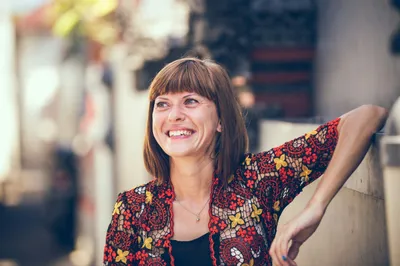 A joyful woman with brown hair smiles brightly, enjoying life outdoors, representing a happy patient in Brisbane after successful cataract surgery.