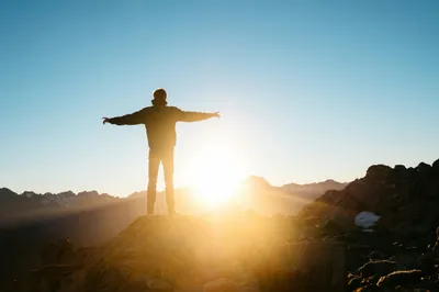 Person on mountain peak at sunrise with arms outstretched, symbolizing clear next-generation vision from PanOptix Pro Lens cataract surgery.