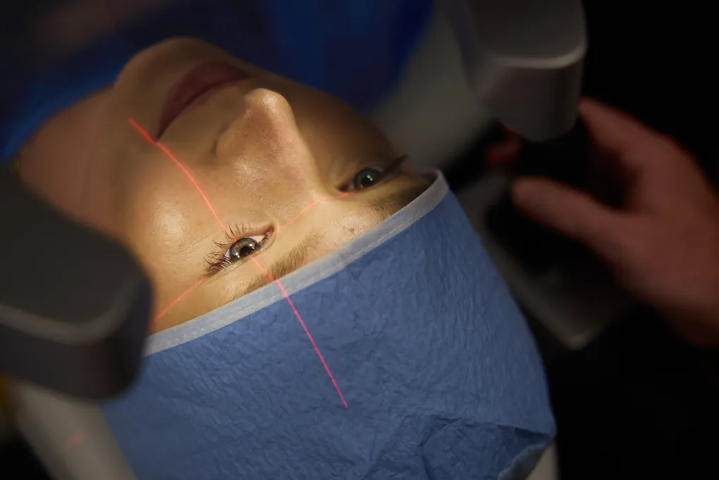 Patient receiving keratoconus eye treatment with red laser light projected onto the cornea, indicative of a modern procedure.