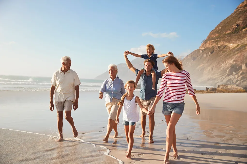 Happy multi-generational family, including active seniors, walking on a sunny beach, symbolizing clear vision and an active lifestyle.
