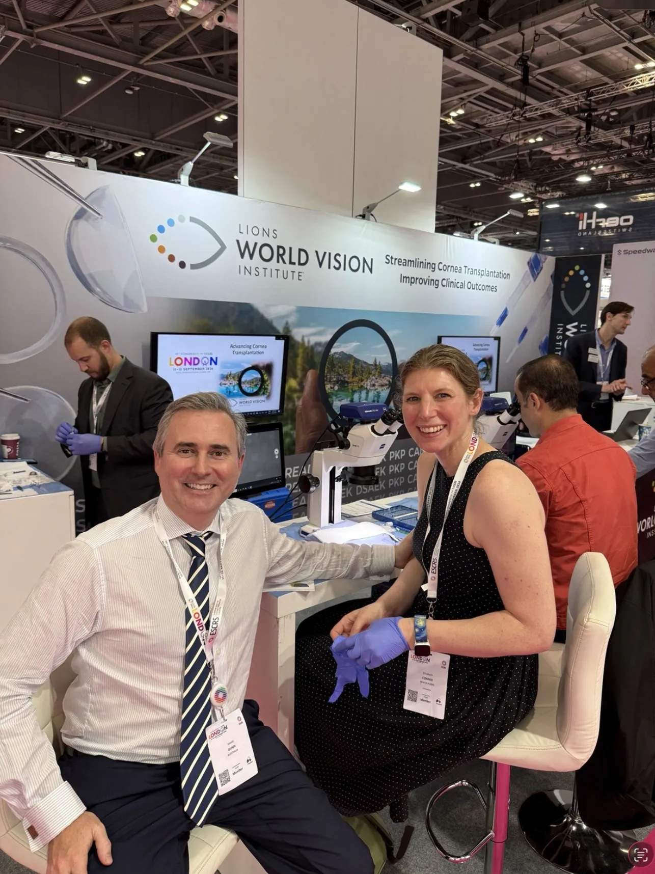 Dr David Gunn teaching at the Lions World Vision Institute CAIRS wet-lab station at ESCRS 2026 with Dr Elizabeth Conner of New Zealand, gloved and seated at the microscope.