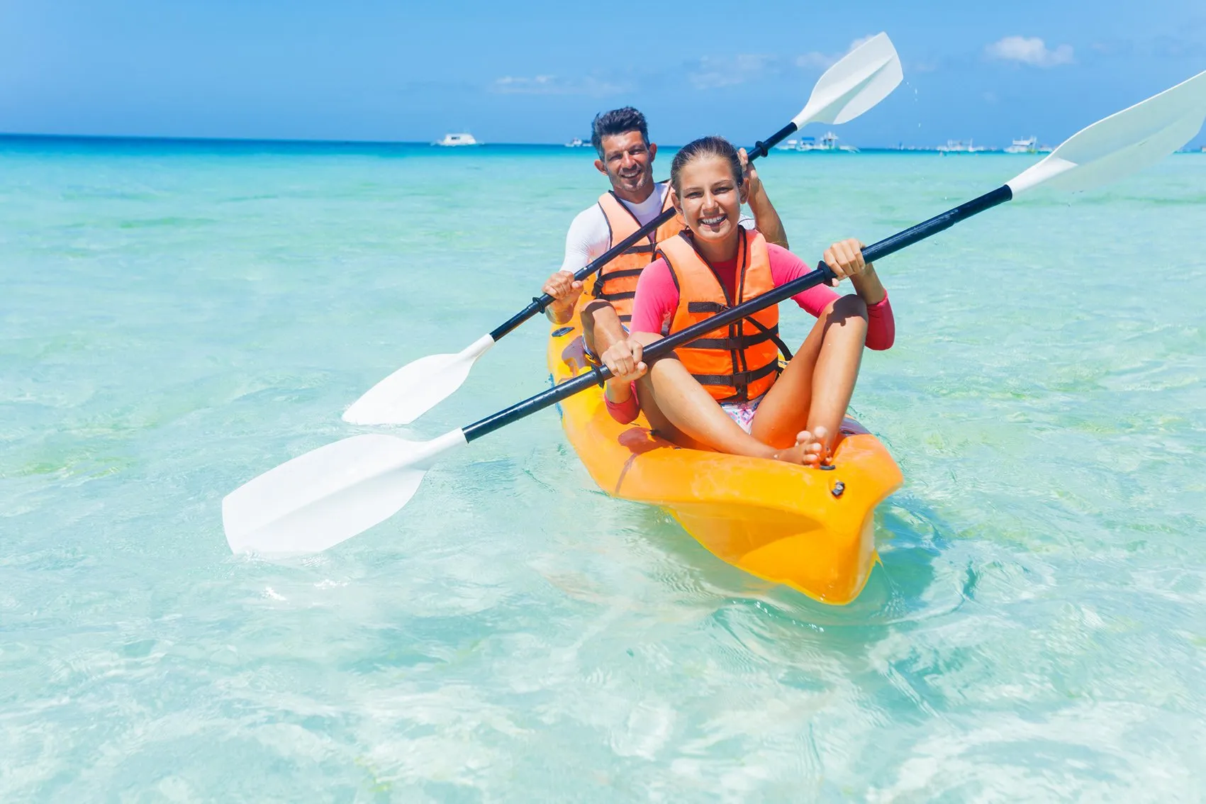 Smiling father and daughter in an orange kayak on sparkling turquoise water, illustrating clear vision and an active post-cataract surgery lifestyle.