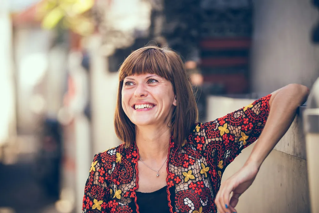 A joyful woman with brown hair smiles brightly, enjoying life outdoors, representing a happy patient in Brisbane after successful cataract surgery.
