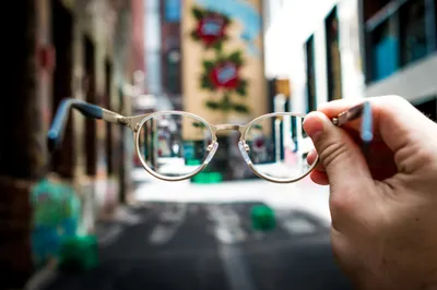 Hand holding prescription eyeglasses against a blurry Brisbane street scene, illustrating vision correction before ICL surgery.