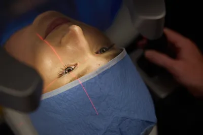 Patient receiving keratoconus eye treatment with red laser light projected onto the cornea, indicative of a modern procedure.