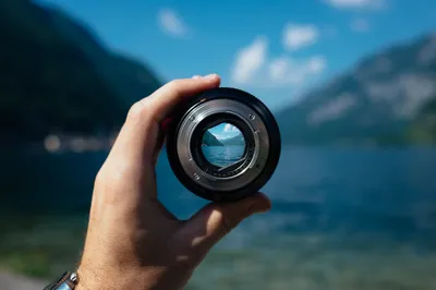 Hand holding camera lens with clear lake reflection, symbolizing improved vision and focus for keratoconus treatment.