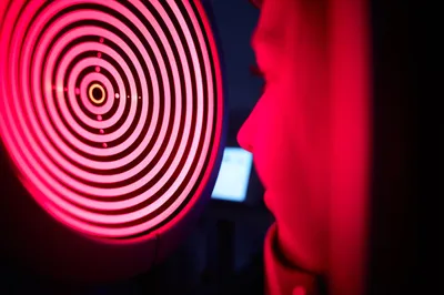 Patient receives a corneal topography exam with a red-lit machine, essential for assessing eye health before cataract or lens replacement surgery.